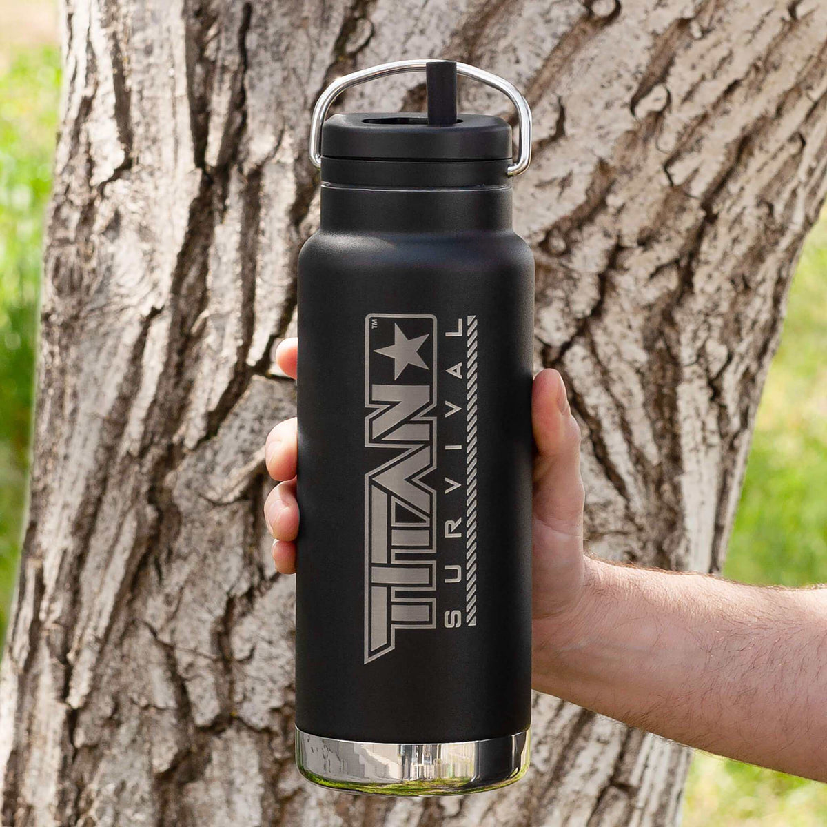 32 Oz wide mouth water bottle with TITAN Survival branding held outdoors.