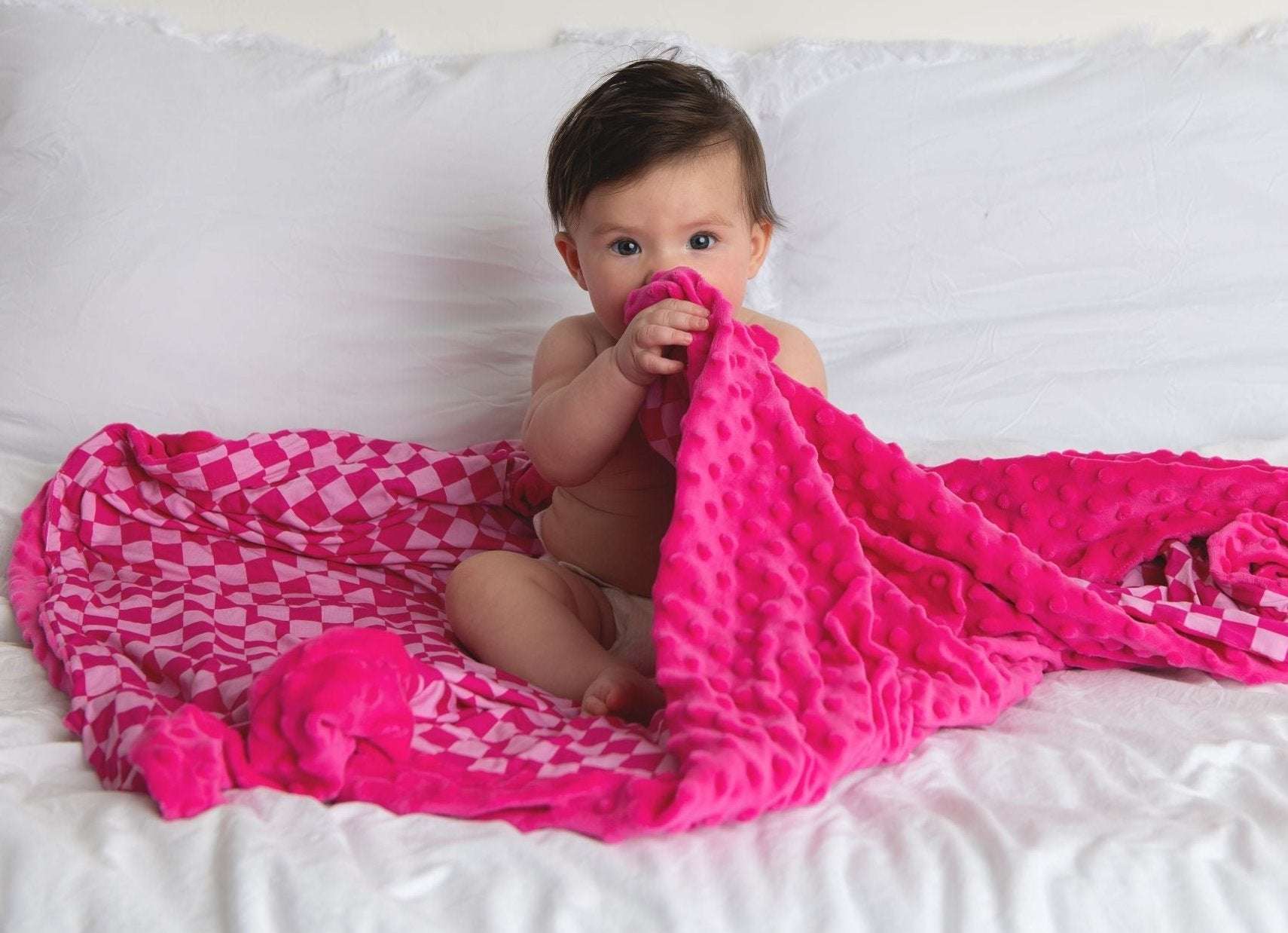 Baby wrapped in pink bamboo minky blanket sitting on white bed