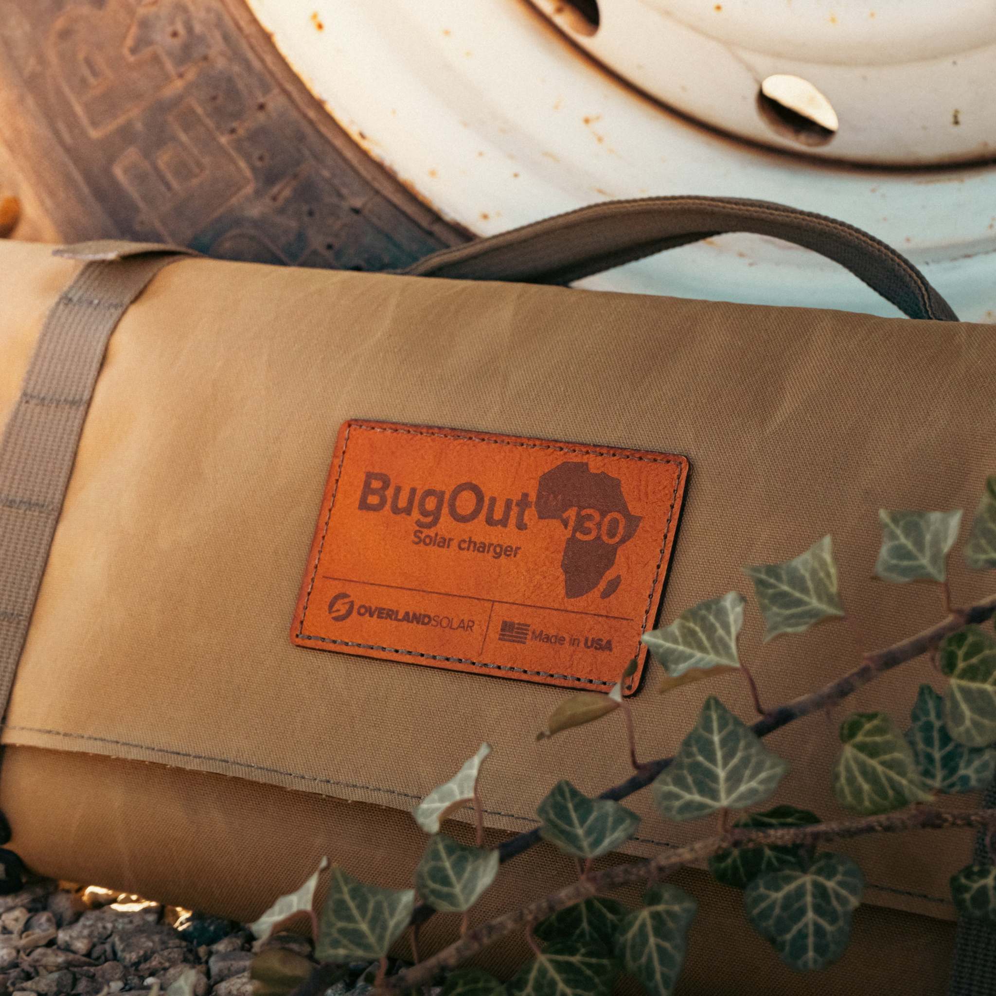 Bugout 130 portable solar charger folded in durable tan waterproof fabric bag next to vehicle tire outdoors