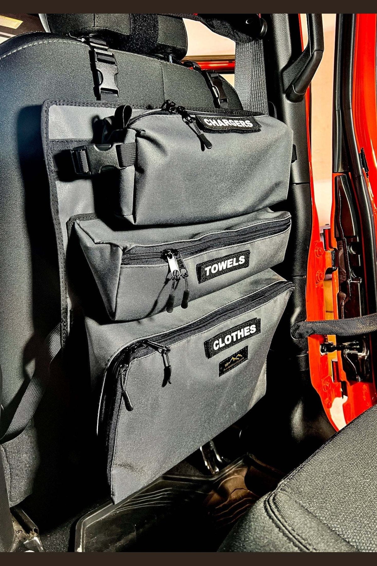 Car seat with Arches Overlander 1 Seat Organizer holding towels and clothes, showcasing storage pockets and quick-release buckles.