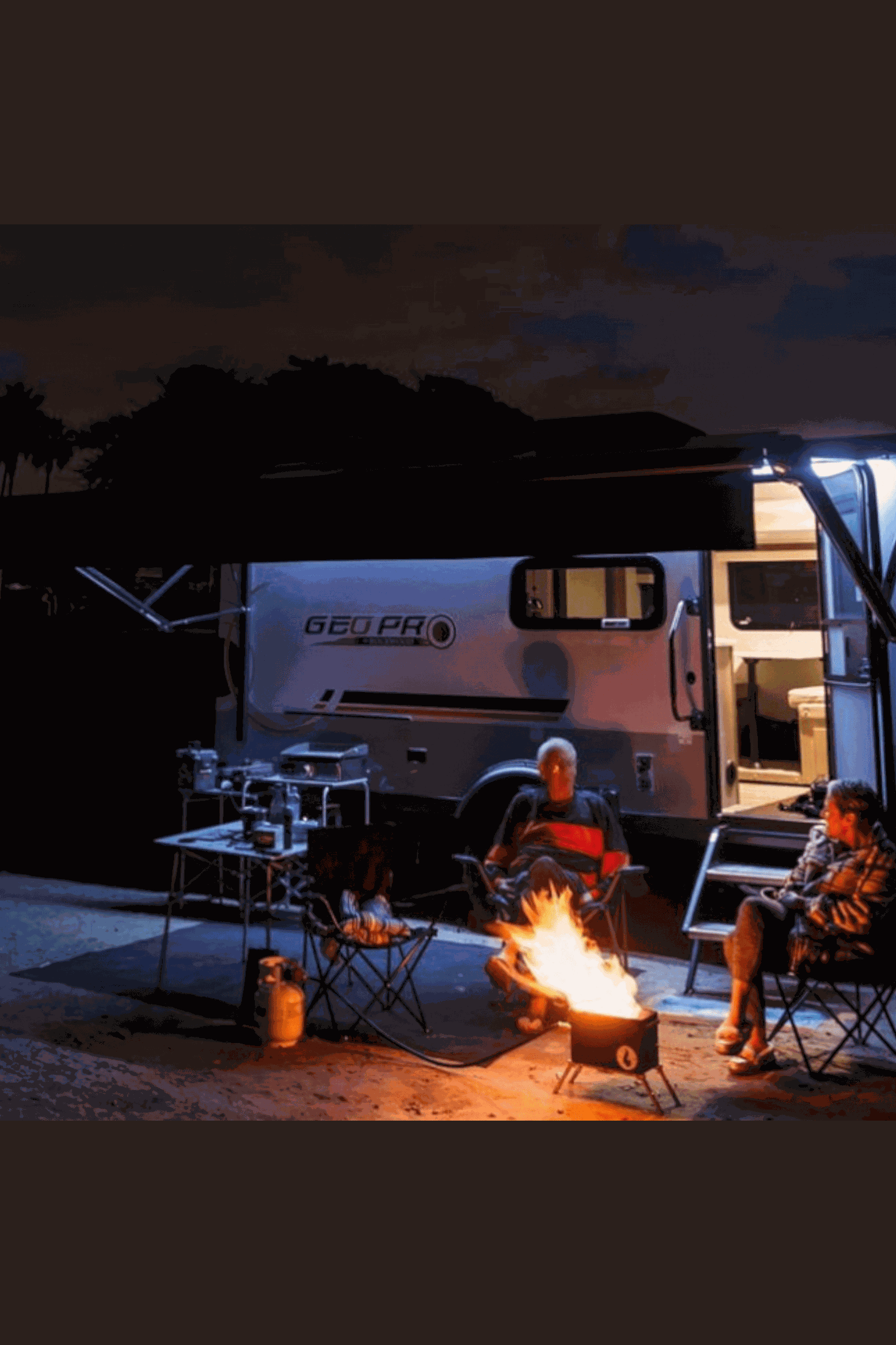 Outdoor camping scene with people enjoying a fire from the Original LavaBox Combo kit next to a camper.