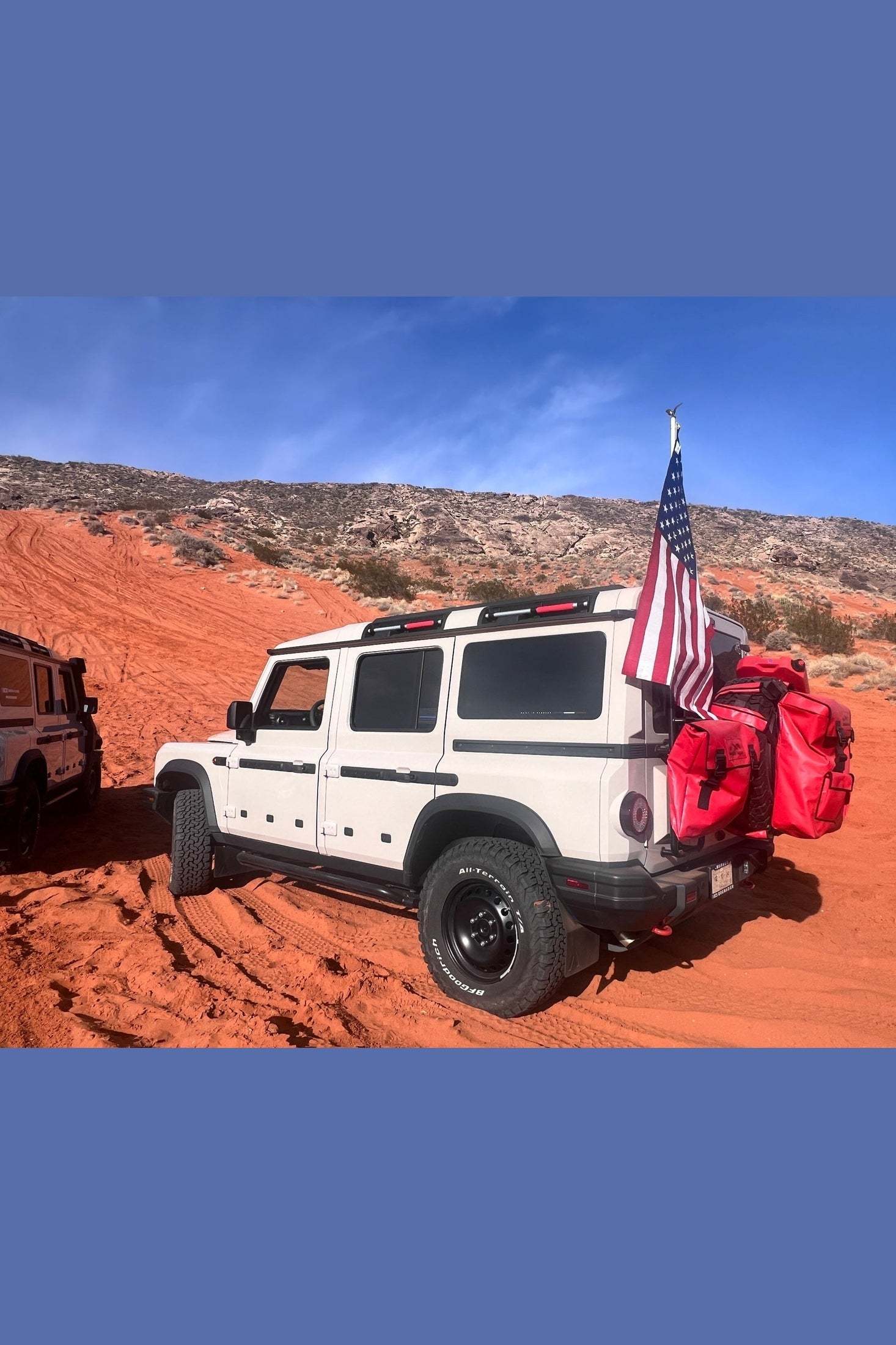 White INEOS Grenadier vehicle equipped with red INEOS Grenadier Adventure Gear Bag Ladder on rugged red dirt terrain