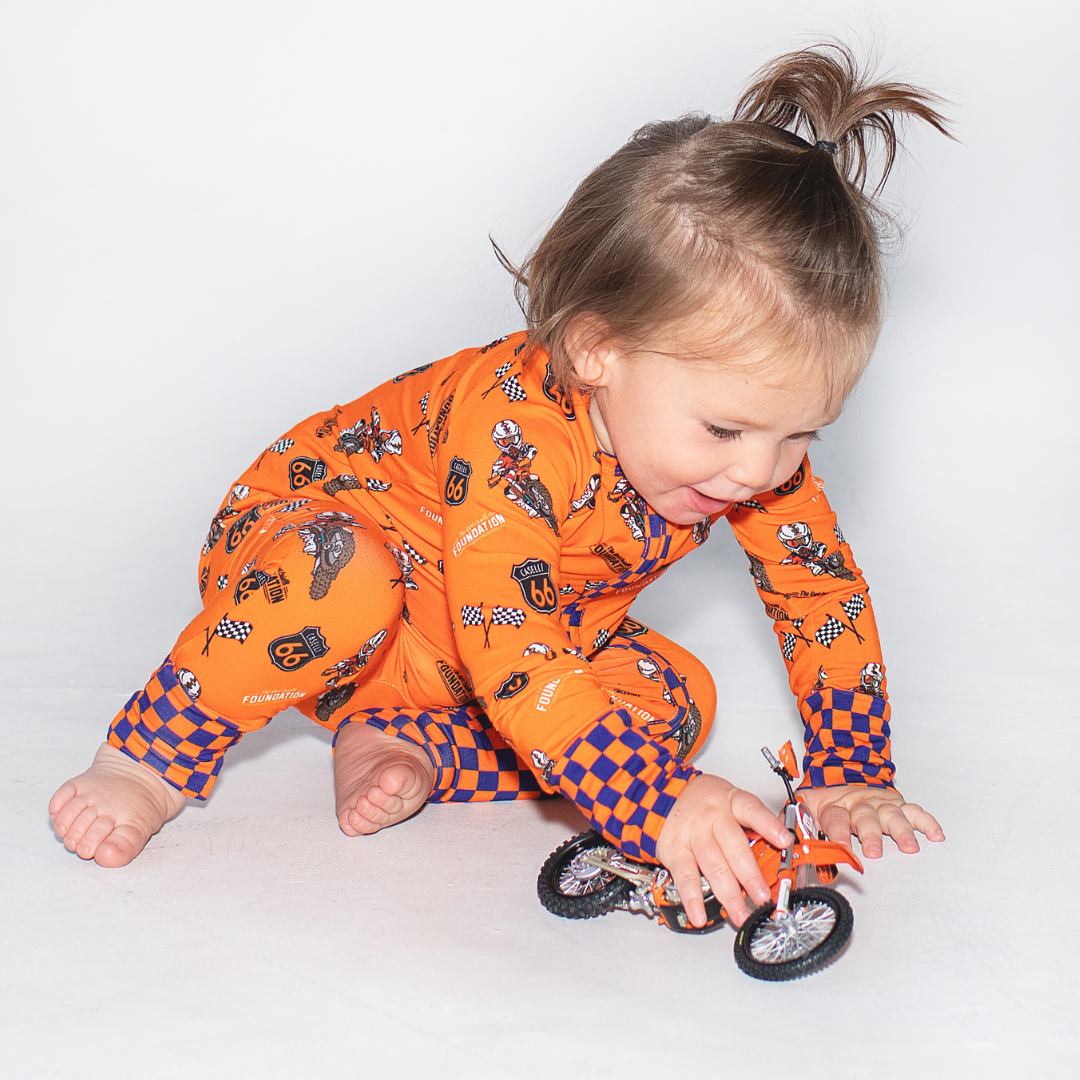 Baby wearing orange Convertible Zippy onesie with motorcycle print playing with toy bike