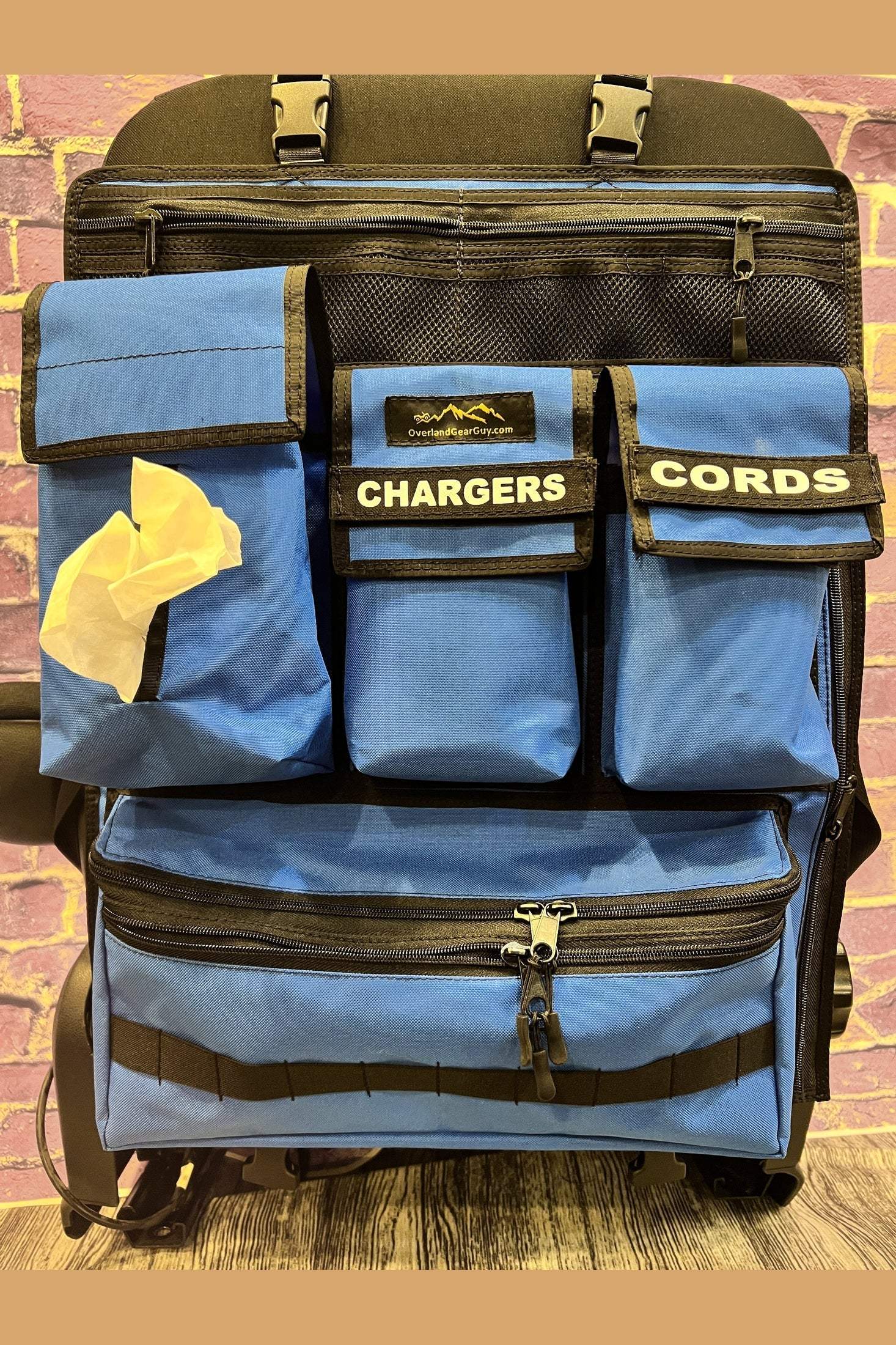 Moab Seat Organizer with multiple labeled pockets for chargers, cords, tissues, and a large zippered compartment attached to a car seat.