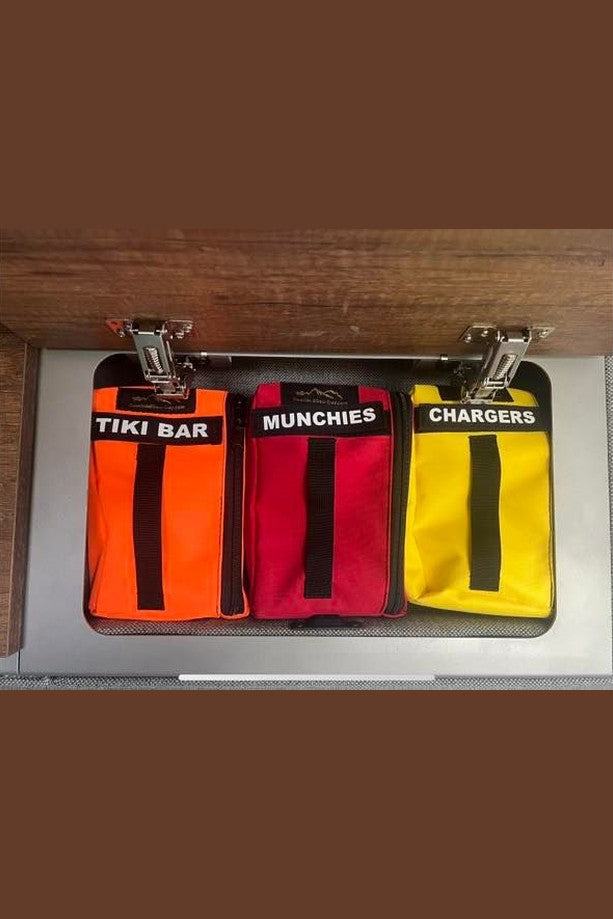 Storyteller Overhead Cabinet Storage Bags in orange, red, and yellow with labeled compartments for tiki bar, munchies, and chargers.