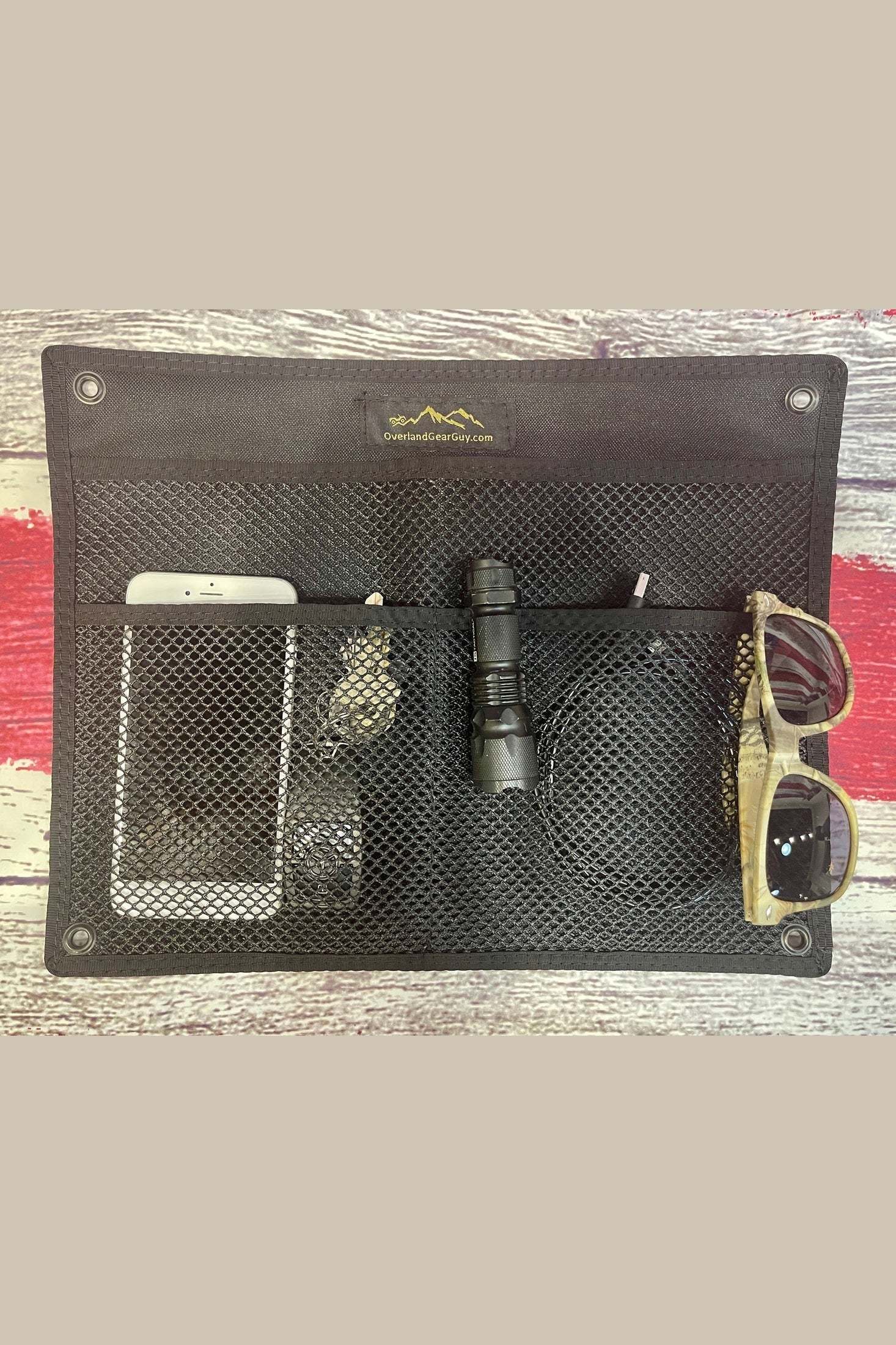 black wall organizational pouch with grommets holding phone, flashlight, sunglasses, and other small items on wooden surface