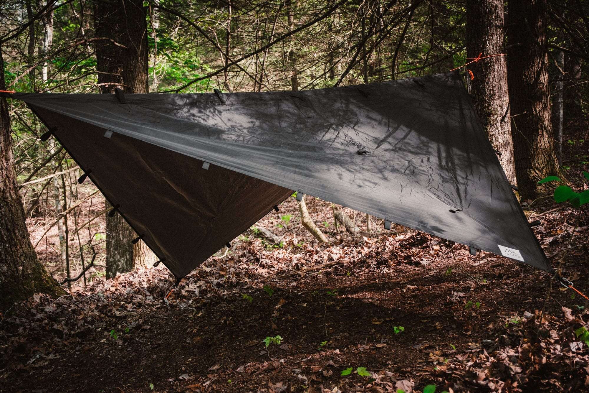 Bushcraft reflective shelter tarp set up in wooded area, showcasing durable construction and versatility.