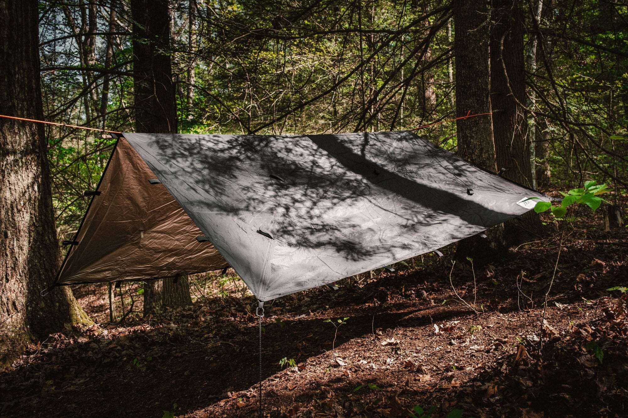 Bushcraft Reflective Shelter Tarp set up in wooded area for outdoor protection.