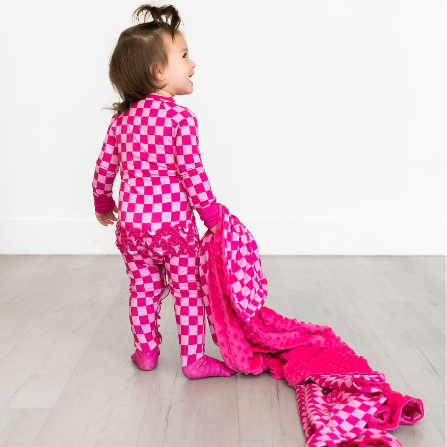 Toddler holding pink reversible bamboo minky blanket with checkerboard pattern