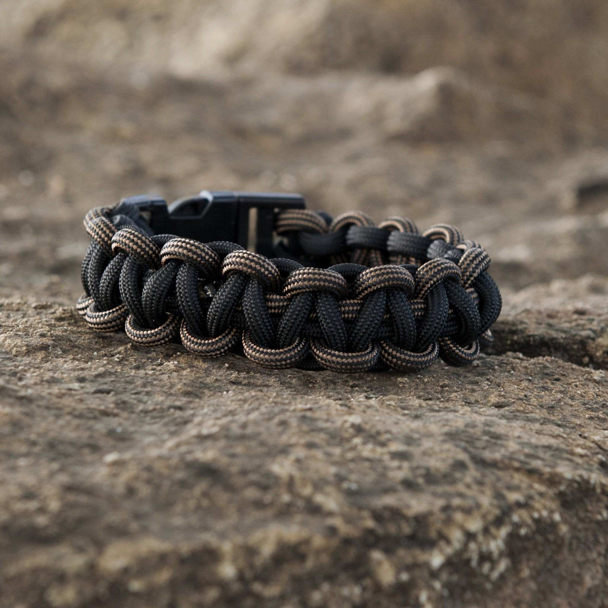 Bronze SurvivorCord bracelet on rocky surface, showcasing durable paracord with integrated survival strands, ideal for outdoor adventures.