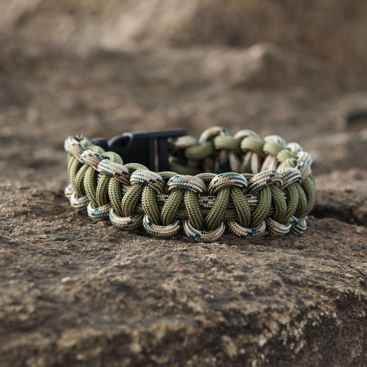 Forest Camo SurvivorCord bracelet on rocky surface, featuring MIL-STYLE 550 paracord with integrated survival strands.