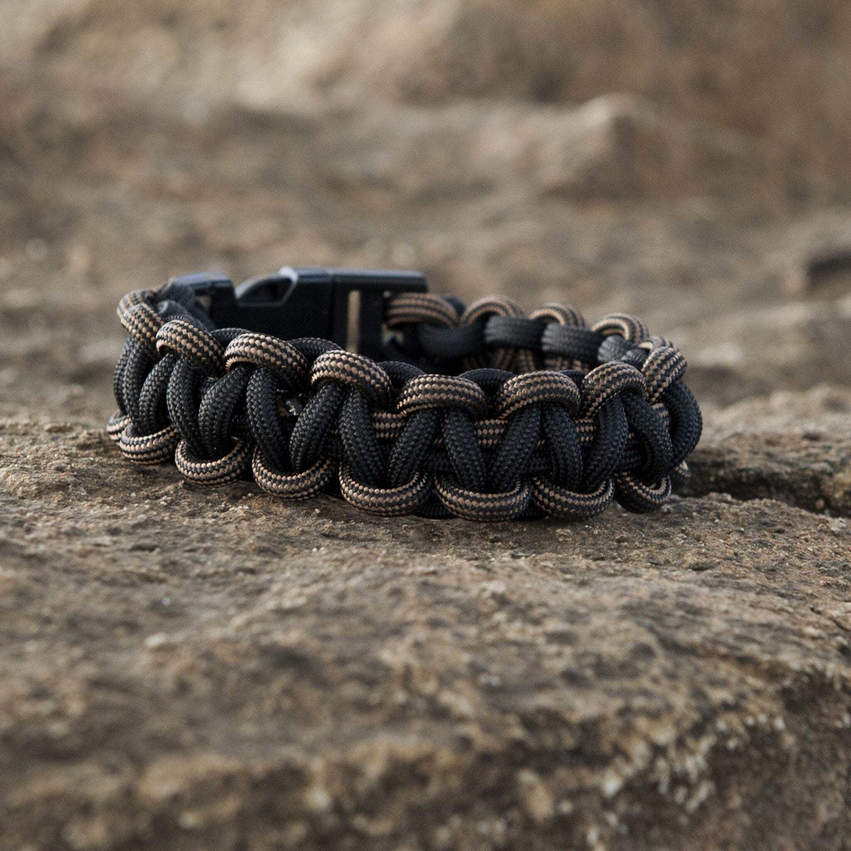 SurvivorCord XT Paracord bracelet on rocky surface, showcasing durable, tactical design with braided strands for survival use.