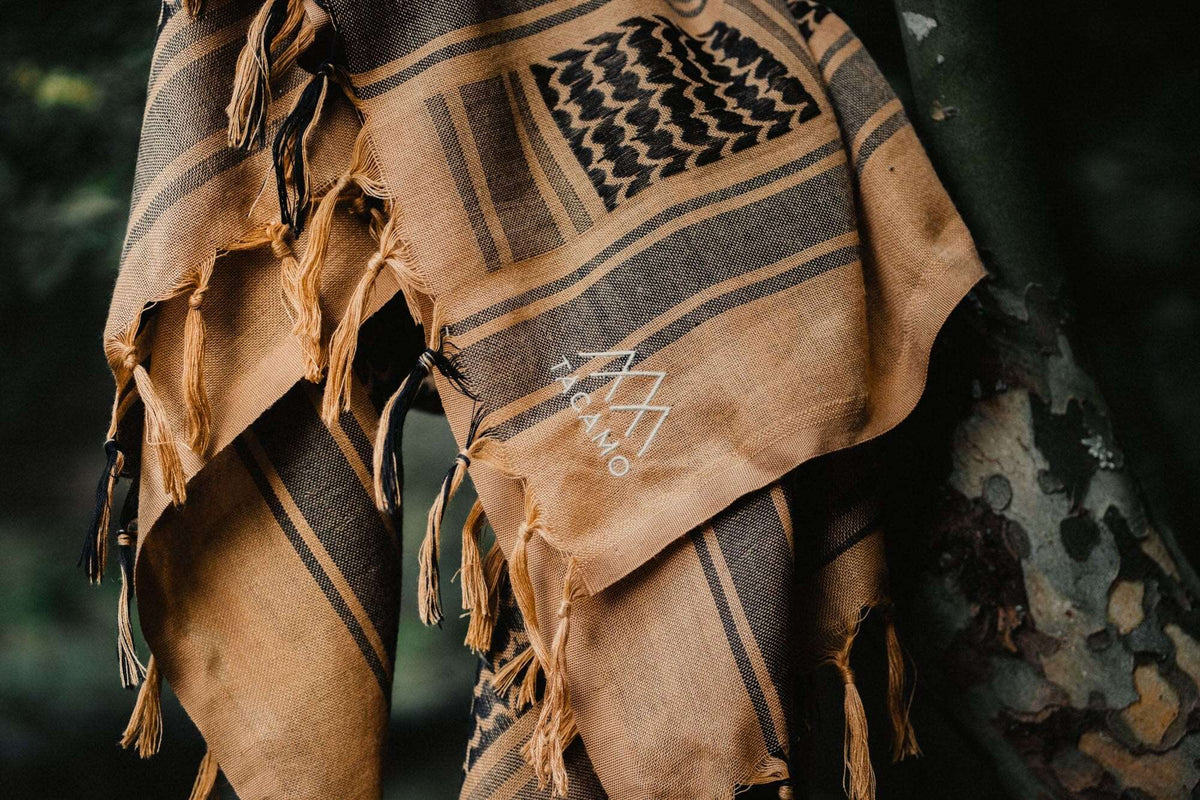 TACAMO® Shemagh Desert Scarf hanging on a tree, showcasing its tactical and stylish keffiyeh design in coyote brown.