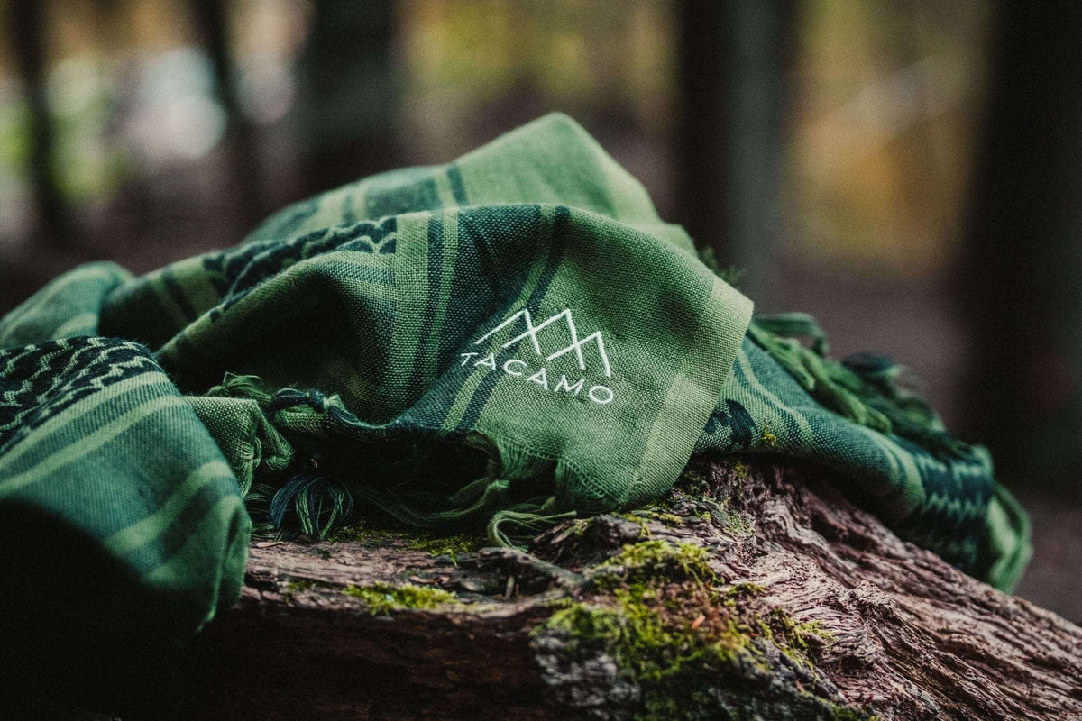 TACAMO Shemagh Desert Scarf draped on mossy wood, showcasing traditional keffiyeh design in green tones.