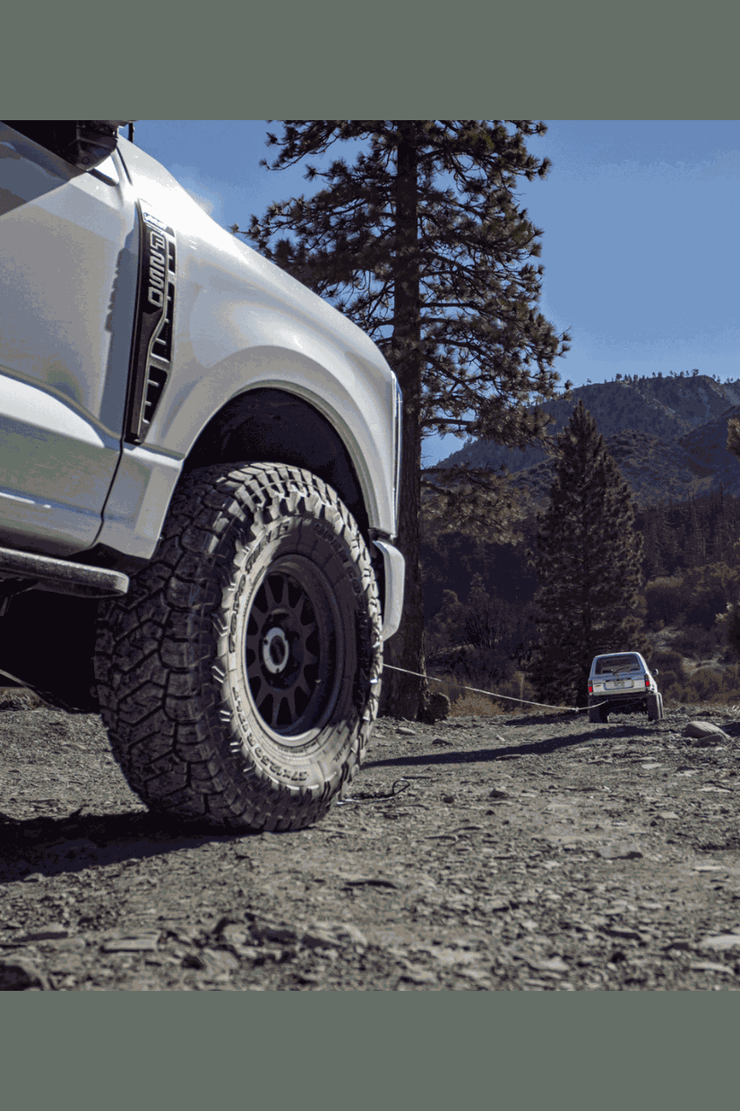 Truck using 50' winch line extension for off-road recovery in rugged terrain.
