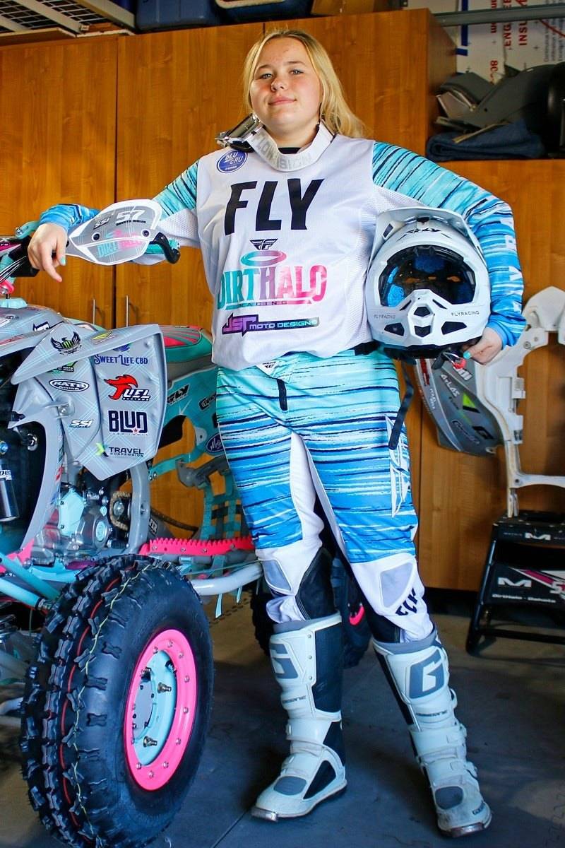 DirtHalo Racing’s Dakota Hibler posing confidently in racing gear with her dirt track race car