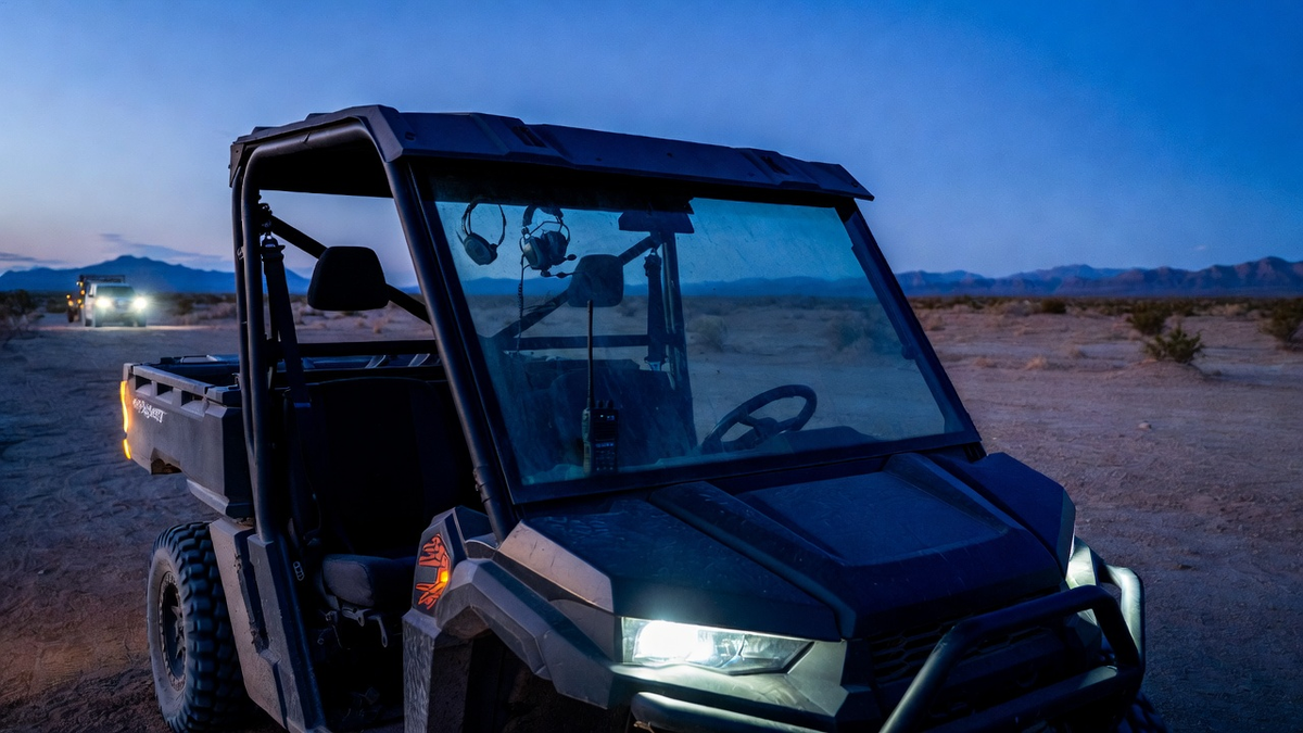Recreational UTV at dusk camp with radio and intercom gear visible — weekend trail crew still on channel