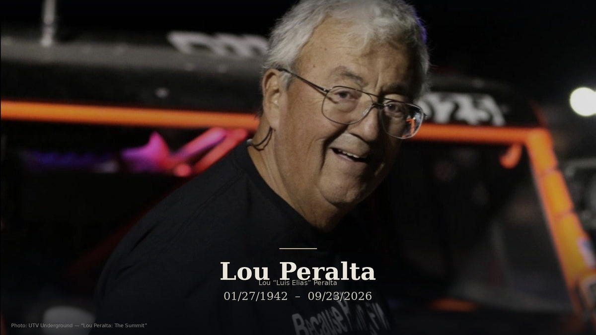 Memorial portrait of Lou Peralta smiling at a night race with soft vehicle lights behind him; muted dark treatment with name and dates 01/27/1942 – 09/23/2026.