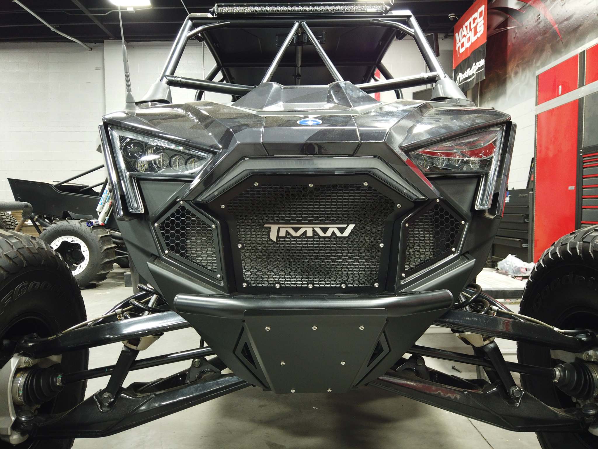 Front view of offroad vehicle featuring black TMW RZR PRO R/XP grill with mesh and logo in a workshop setting