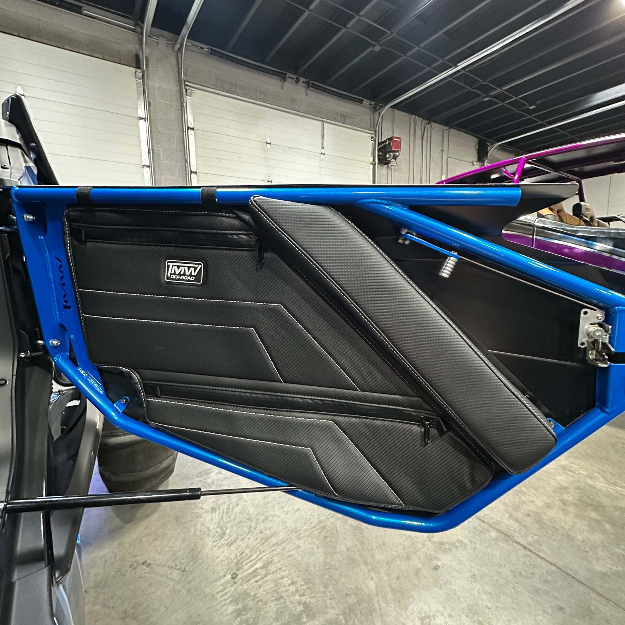 TMW Maverick R black carbon fiber door bag with two spacious pockets and built-in knee pad on blue off-road vehicle door