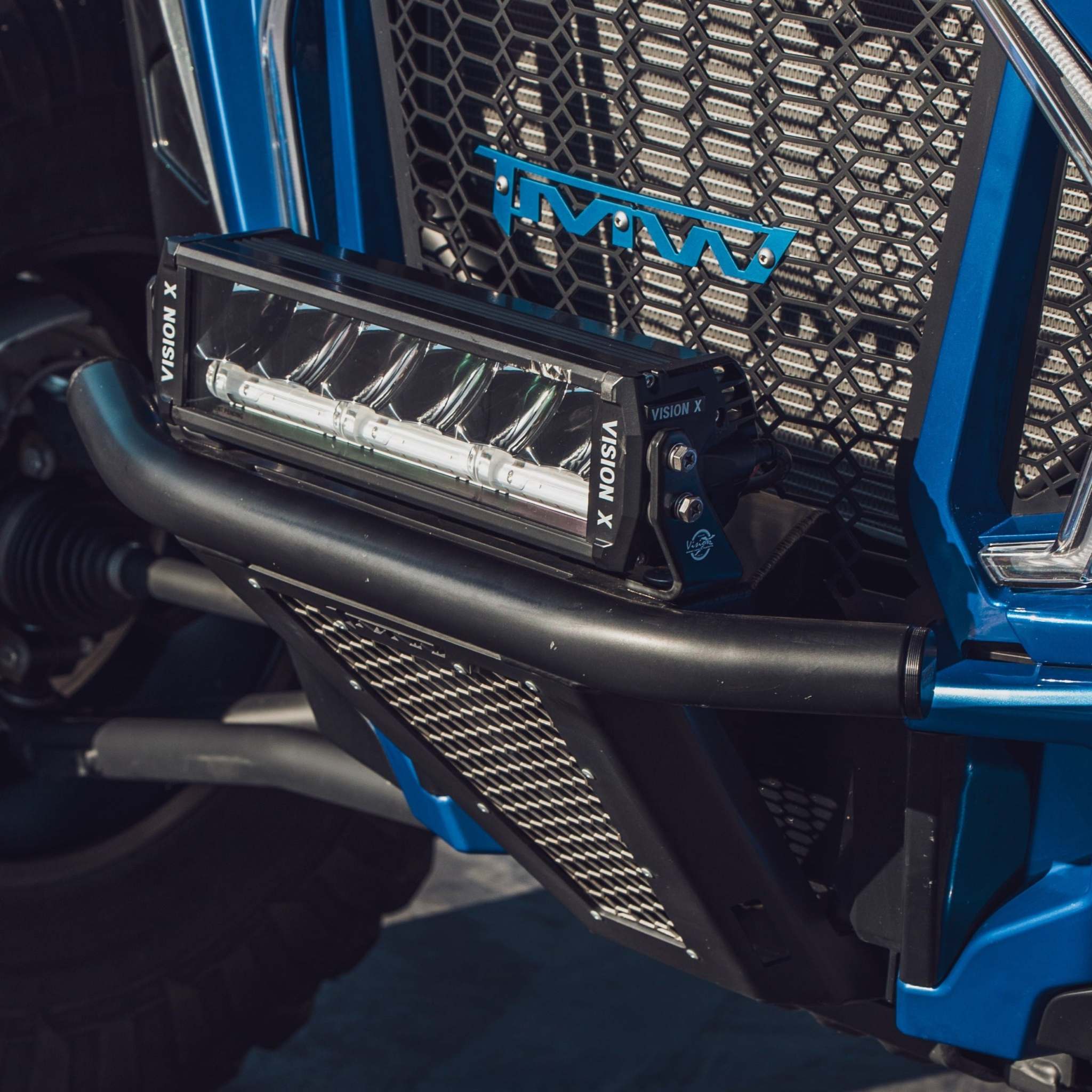 Close-up of TMW Baja RZR Front Bumper in semi gloss black with 304 stainless steel mesh and Vision X light bar on blue RZR vehicle