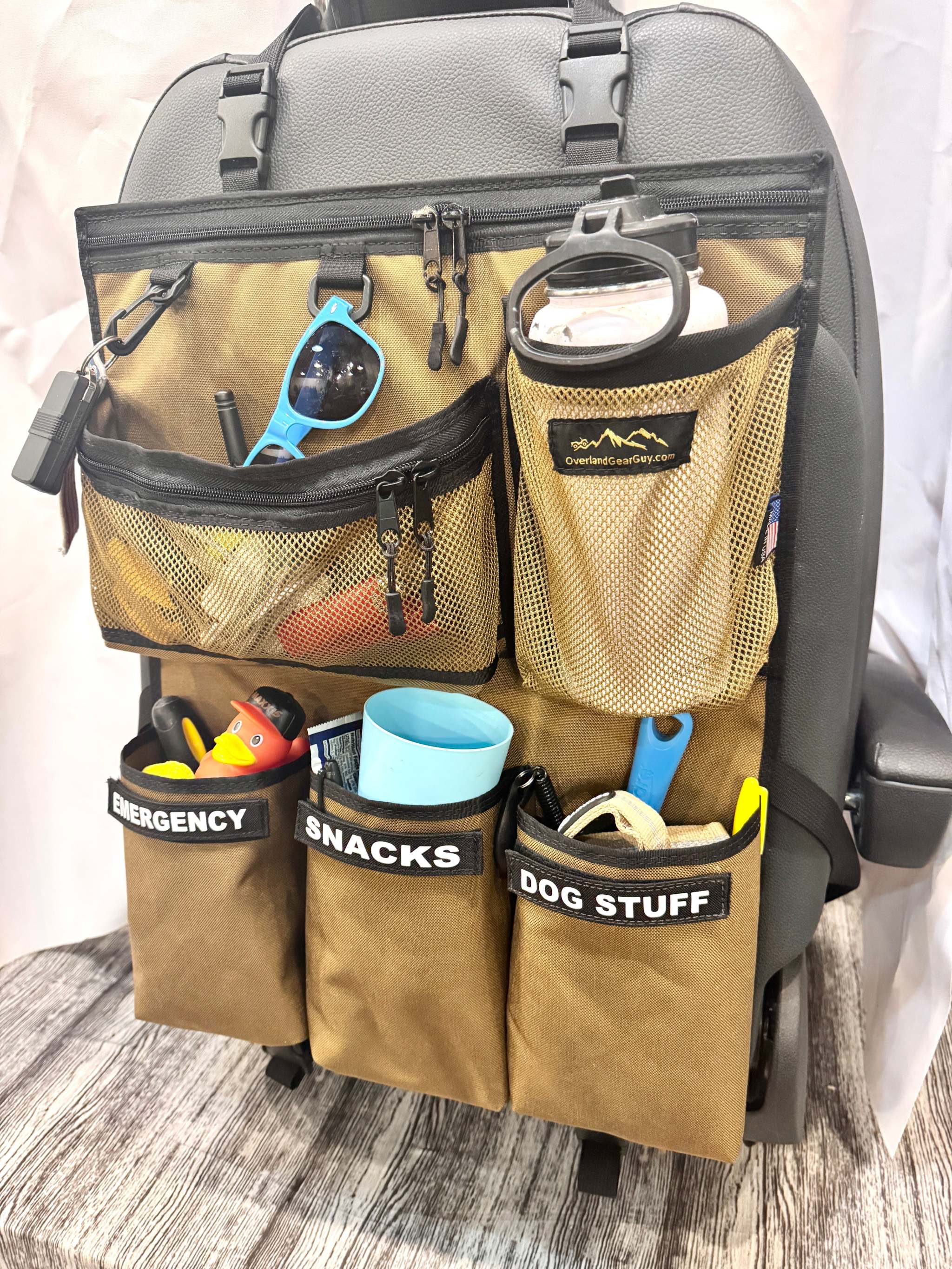 Voyager Seat Organizer hanging on car seat with multiple labeled pockets for emergency, snacks, and dog supplies