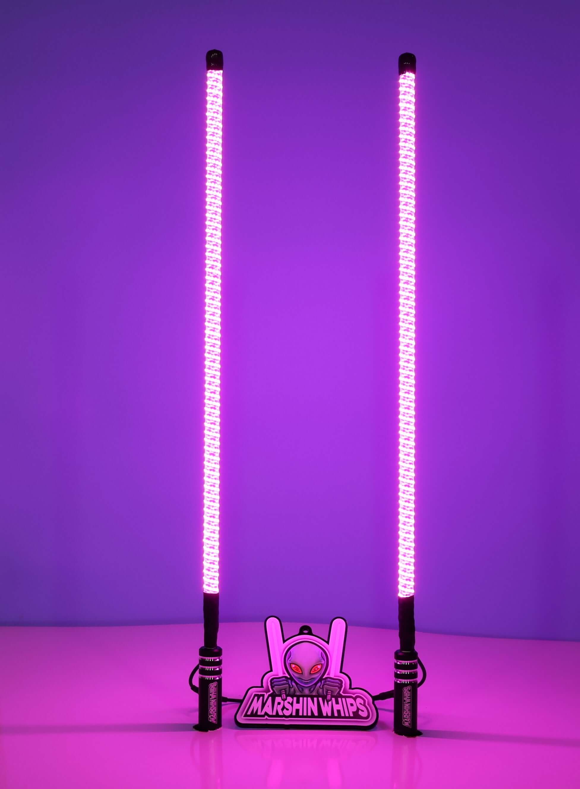 Pair of V2 Whips off-road LED light sticks glowing bright pink with black powder-coated bases and magnetic mounts.