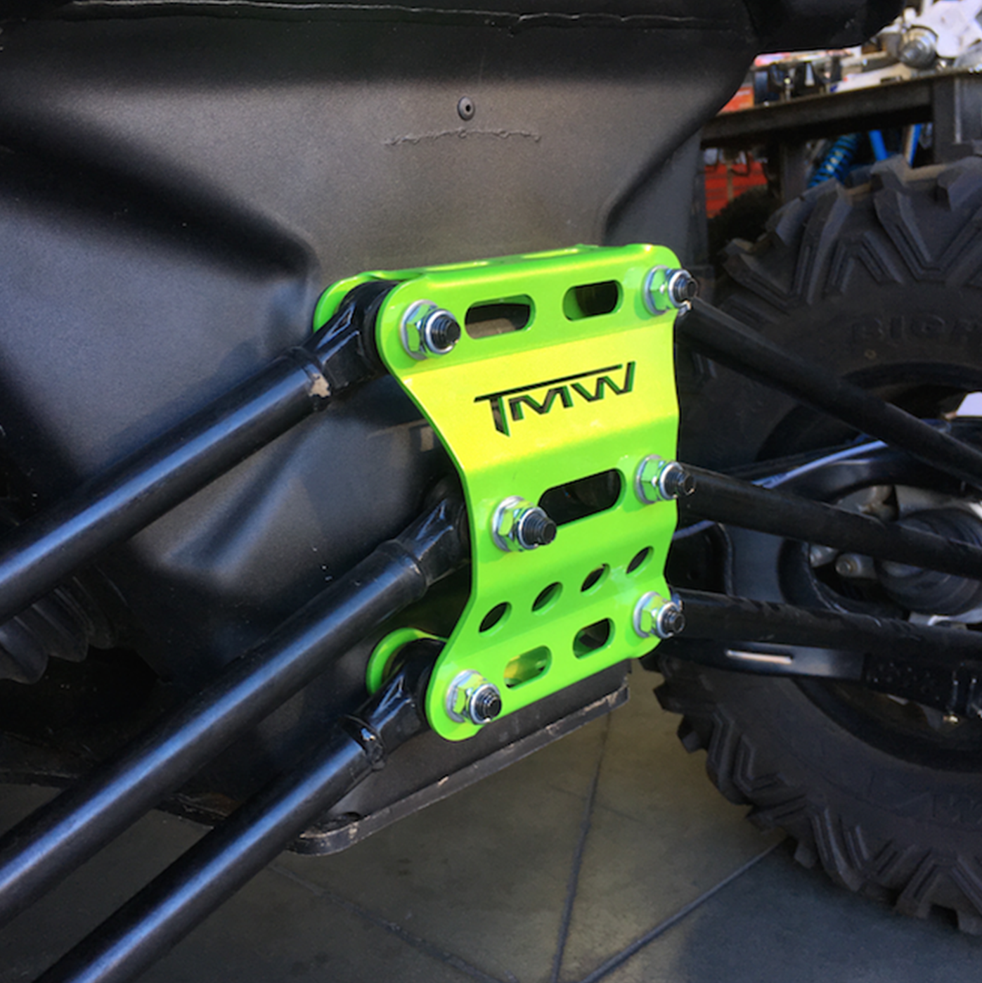 Bright green TMW rear radius rod gusset plate mounted on offroad vehicle frame for CanAm X3, reinforced with multiple bolts for added strength.