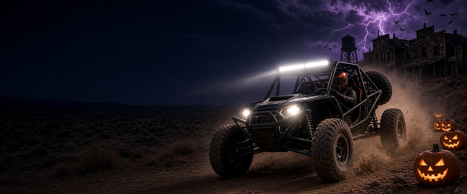 Black tube-cage desert buggy with an orange-helmeted driver charging past jack-o'-lanterns and a ghost town under purple lightning